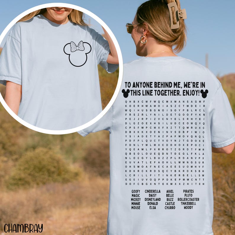 May include: Light blue t-shirt featuring a Minnie Mouse outline on the front and text on the back that reads "TO ANYONE BEHIND ME, WE'RE IN THIS LINE TOGETHER. ENJOY!" with a word search of Disney characters.