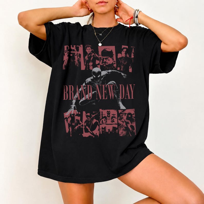 May include: A black short-sleeved t-shirt featuring a graphic print with multiple panels of comic book characters and the text BRAND NEW DAY in a muted red font. The central image depicts a masked figure in a crouched pose on the front of the shirt.