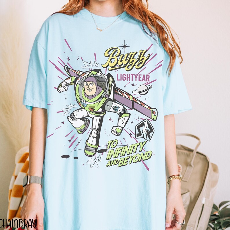 Puede incluir: Camiseta azul claro con un dise&ntilde;o de Buzz Lightyear. El dise&ntilde;o incluye el texto "Buzz Lightyear" y "To Infinity and Beyond". La imagen de dibujos animados es en verde, blanco, morado y negro. Una camiseta divertida e informal.
