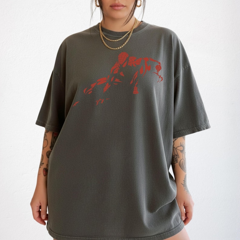 May include: A charcoal gray oversized t-shirt featuring a bold, red graphic print of a crouching figure on the chest. The garment has a crew neckline, short sleeves, and a relaxed fit, providing a simple and clean look for casual daily wear.