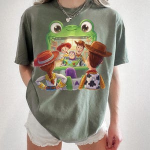 Puede incluir: Camiseta verde oliva con un dise&ntilde;o gr&aacute;fico colorido de personajes de la pel&iacute;cula animada Toy Story. El dise&ntilde;o incluye a Woody, Buzz Lightyear, Jessie y otros personajes. La camiseta tiene mangas cortas.