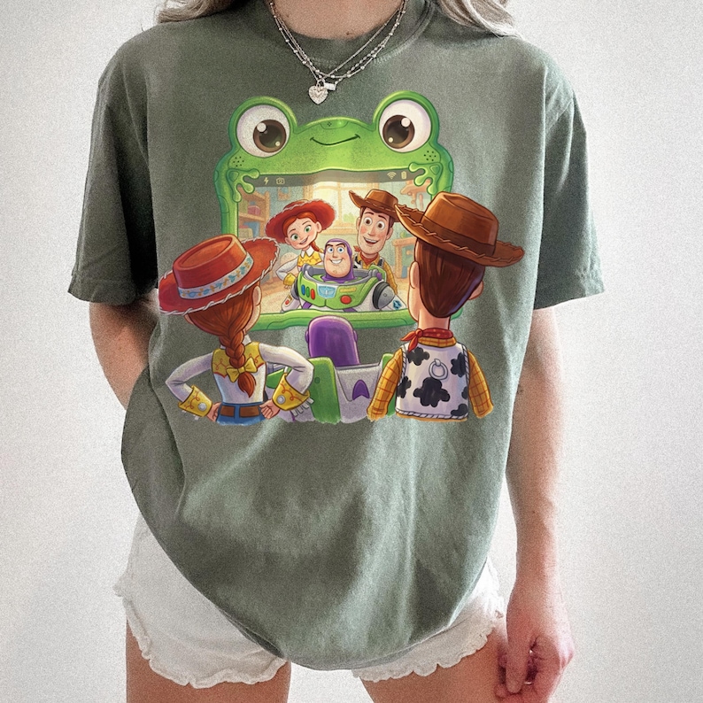 Puede incluir: Camiseta verde oliva con un dise&ntilde;o gr&aacute;fico colorido de personajes de la pel&iacute;cula animada Toy Story. El dise&ntilde;o incluye a Woody, Buzz Lightyear, Jessie y otros personajes. La camiseta tiene mangas cortas.