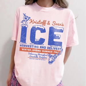 May include: A light pink t-shirt featuring the text "Kristoff & Sven's ICE" in blue and red, with a distressed effect. The shirt also includes graphics of Olaf and Sven, and the text "Harvesting and Delivery."