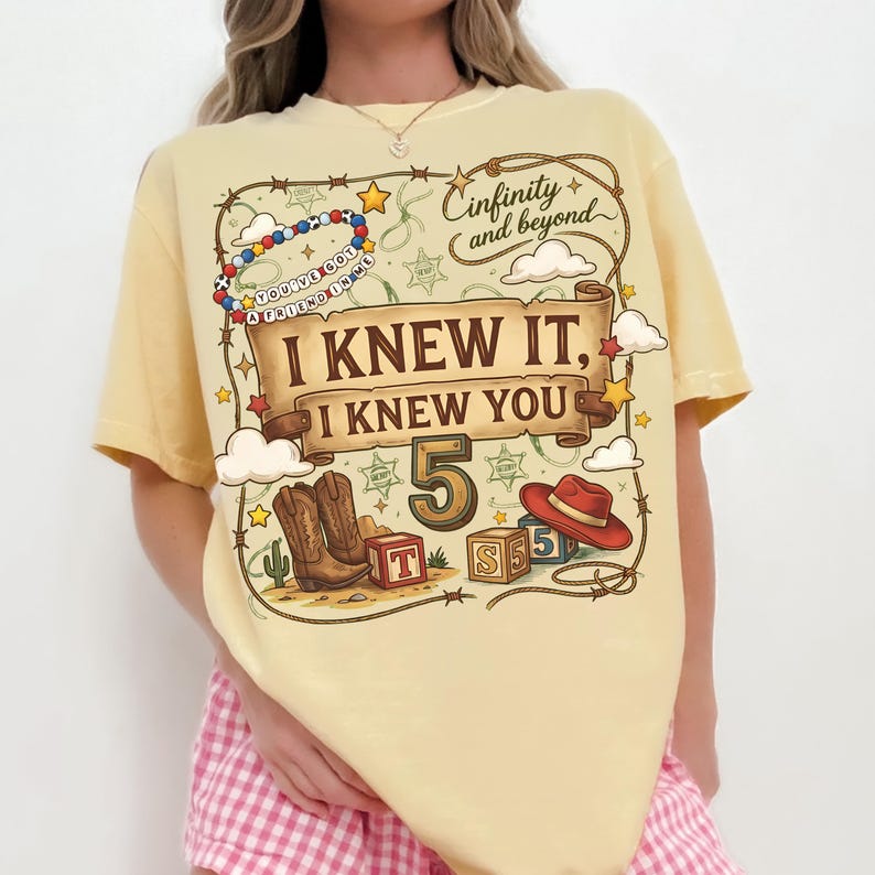 May include: A pale yellow t-shirt featuring a graphic print with a lasso border, a scroll banner reading I KNEW IT, I KNEW YOU, a large number 5, cowboy boots, a red hat, alphabet blocks, and the text Cinfinity and beyond and YOU'VE GOT A FRIEND IN ME.