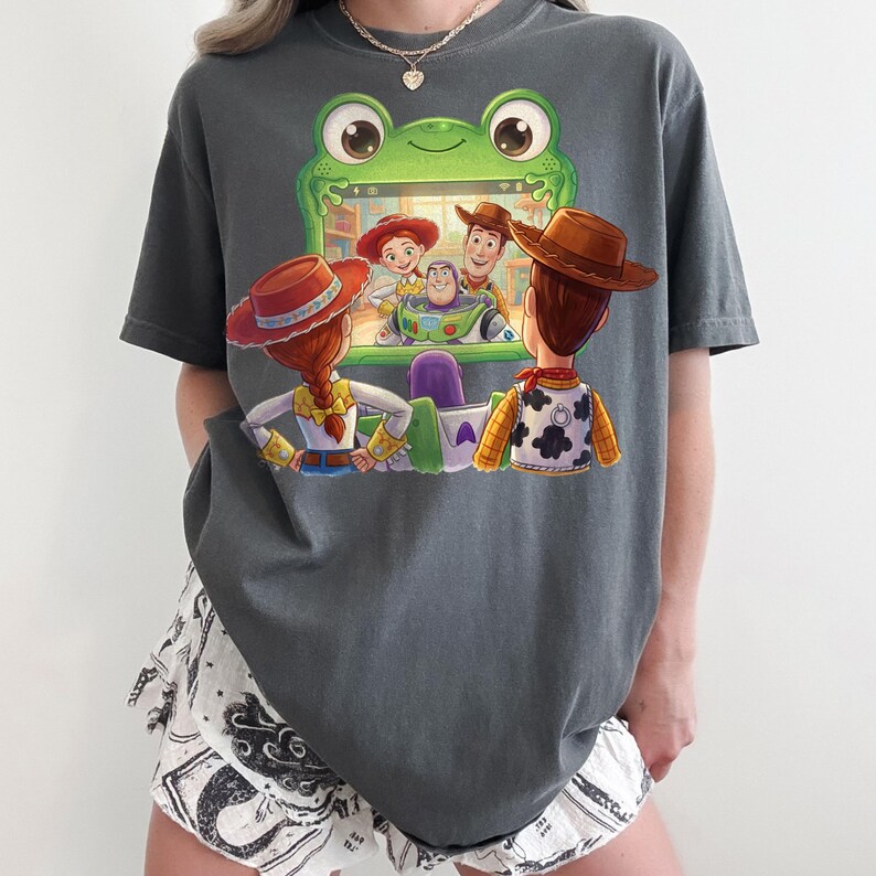 Puede incluir: Camiseta gris oscuro con un gr&aacute;fico colorido de personajes de la pel&iacute;cula animada "Toy Story". El dise&ntilde;o muestra a Woody, Buzz Lightyear, Jessie y otros personajes mirando una pantalla. La camiseta es de corte holgado.
