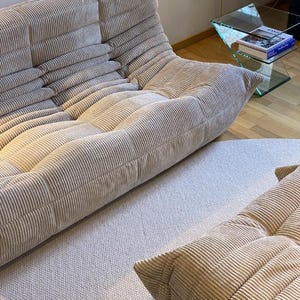 May include: Beige corduroy modular sofa with a low profile and rounded cushions. The sofa is composed of multiple sections, creating a comfortable and inviting seating arrangement. The fabric has a ribbed texture.