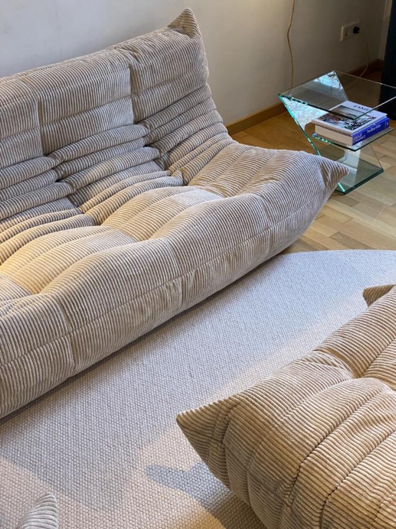 May include: Beige corduroy modular sofa with a low profile and rounded cushions. The sofa is composed of multiple sections, creating a comfortable and inviting seating arrangement. The fabric has a ribbed texture.