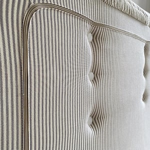 May include: Close-up of a headboard with a striped pattern in off-white and gray. The headboard features a button-tufted design and a decorative trim. The fabric has a textured appearance, and the overall aesthetic is classic and elegant.