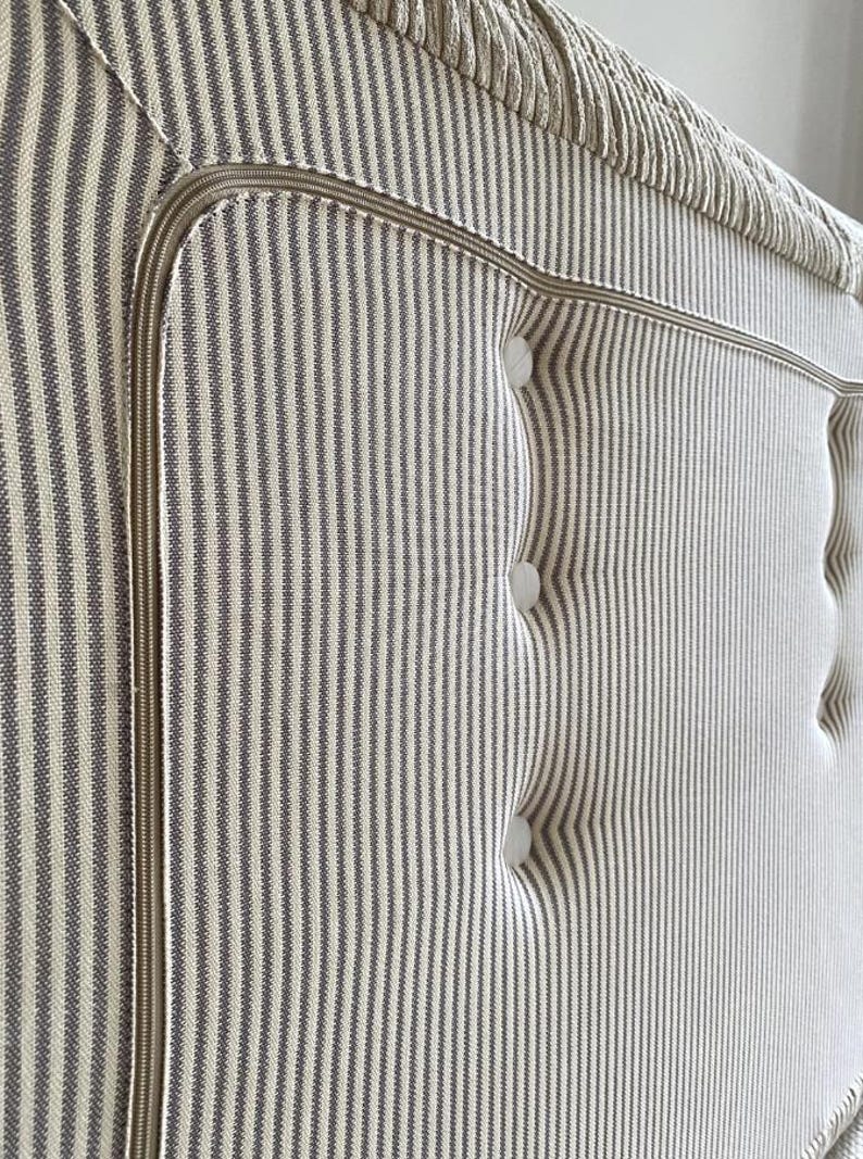 May include: Close-up of a headboard with a striped pattern in off-white and gray. The headboard features a button-tufted design and a decorative trim. The fabric has a textured appearance, and the overall aesthetic is classic and elegant.