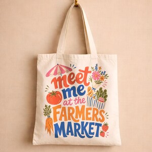 May include: A cream-colored canvas tote bag featuring a colorful graphic print with the text "meet me at the FARMERS MARKET". The design includes illustrations of a pink and white striped umbrella, a bouquet of flowers, a tomato, carrots, and strawberries.