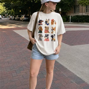 Puede incluir: Una camiseta de manga corta color hueso con una cuadr&iacute;cula de nueve retratos de perros ilustrados, cada uno con un accesorio diferente como un pa&ntilde;uelo, un su&eacute;ter o un lazo. La prenda se combina con pantalones cortos de mezclilla azul claro.