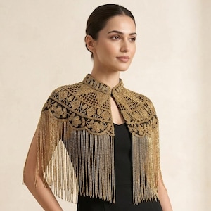 May include: A gold beaded capelet featuring intricate embroidery and a high collar. The garment is adorned with long, dangling gold fringe that extends from the scalloped hemline, layered over a simple black sleeveless dress.