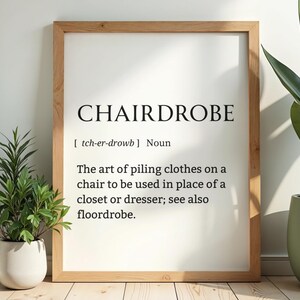 Peut inclure: Impression encadrée avec le mot "CHAIRDROBE" en gras, en noir. La définition décrit l'art d'empiler des vêtements sur une chaise. Le cadre est de couleur marron clair, et le fond est blanc.