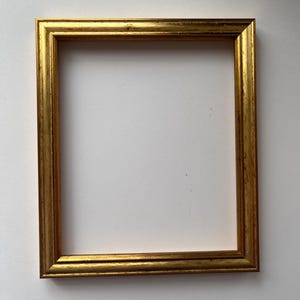 May include: A rectangular gold picture frame with a textured surface. The frame is empty, with a white background visible through the opening. The frame is made of wood and has a classic design.