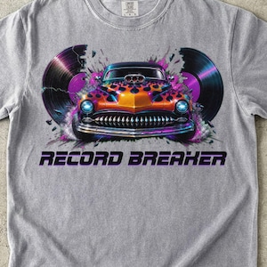 Pode incluir: Uma t-shirt cinzenta com um gráfico de um carro clássico com chamas cor de laranja e roxas, ladeado por dois discos de vinil pretos. O texto "RECORD BREAKER" está impresso em letras pretas a negrito por baixo do carro. Gola redonda e mangas curtas.
