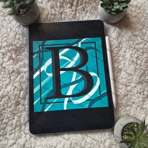 May include: A black tablet shows a teal and white design with the letter "B". The design has a black outline and white swirls. A white stylus is next to the tablet, and small potted plants are in the background.