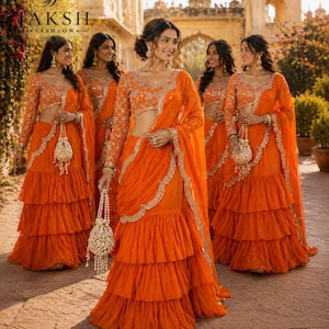 May include: A vibrant orange lehenga set featuring a long-sleeved blouse with intricate silver embroidery, a tiered ruffled skirt, and a matching dupatta with scalloped edges. The ensemble is paired with a beaded drawstring pouch bag.