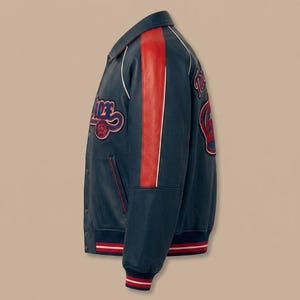 May include: A navy blue varsity jacket with red and white accents. The jacket features a red stripe down the sleeve and patches with text. The cuffs and hem have red and white striped detailing.