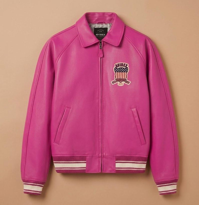 May include: A vibrant fuchsia leather jacket with a classic bomber silhouette. Features a collared neckline, zip-up front, and ribbed cuffs and hem with white stripes. An embroidered patch with an American flag design is on the chest.