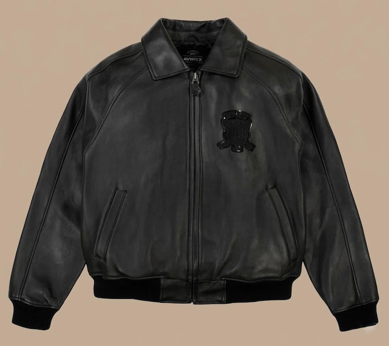 May include: Black leather jacket with a collared neckline, a zipper closure, and a patch on the chest. The jacket has two front pockets and ribbed cuffs and hem. The brand name "AVIREX" is visible on the collar.