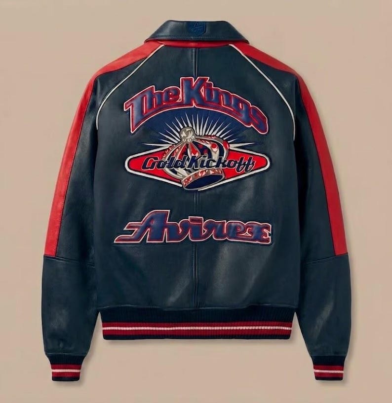 May include: A navy blue leather jacket with red accents on the sleeves and collar. The back features an embroidered design with the text "The Kings", "Gold Kickoff", and "Avirex". The jacket has a ribbed hem and cuffs with red and white stripes.