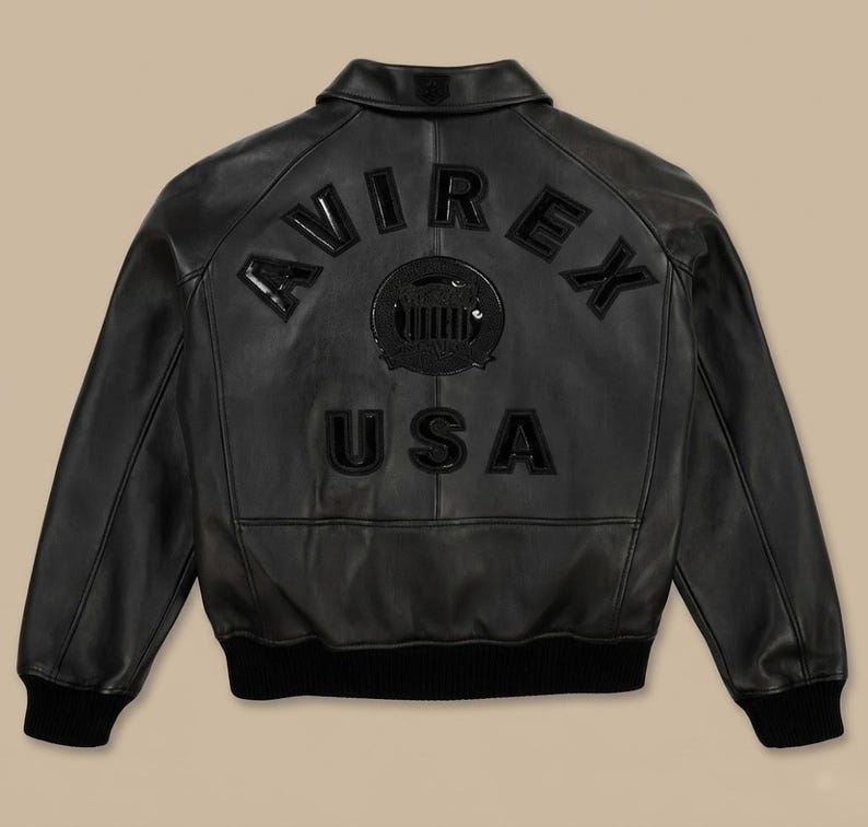 May include: Black leather jacket with the word "AVIREX" arched across the upper back, and "USA" below a circular emblem. The jacket has a collar, ribbed cuffs, and a ribbed hem. The jacket is a classic bomber style.
