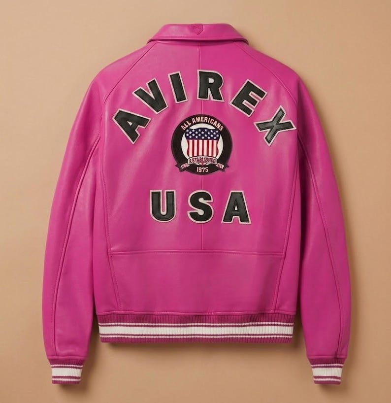 May include: A vibrant pink leather jacket with the word "AVIREX" arched across the shoulders. Below, a circular patch displays a US flag design and the text "ALL AMERICANS ESTABLISHED 1975". The word "USA" is printed below the patch. The jacket has white and burgundy striped cuffs.