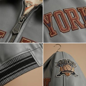 K&ouml;nnte beinhalten: Graue Lederjacke mit dem Wort "YORK" in Braun und Orange gestickt. Die Jacke hat einen Rei&szlig;verschluss, gestreifte Manschetten und einen "New York Knicks"-Patch mit einem Basketball-Logo.