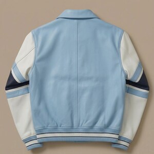 Puede incluir: Una chaqueta universitaria de color azul claro con mangas de cuero blanco y detalles de rayas en azul marino y azul claro. La chaqueta cuenta con un cuello cl&aacute;sico, dobladillo acanalado y pu&ntilde;os acanalados con rayas azul marino y blancas, vista trasera.
