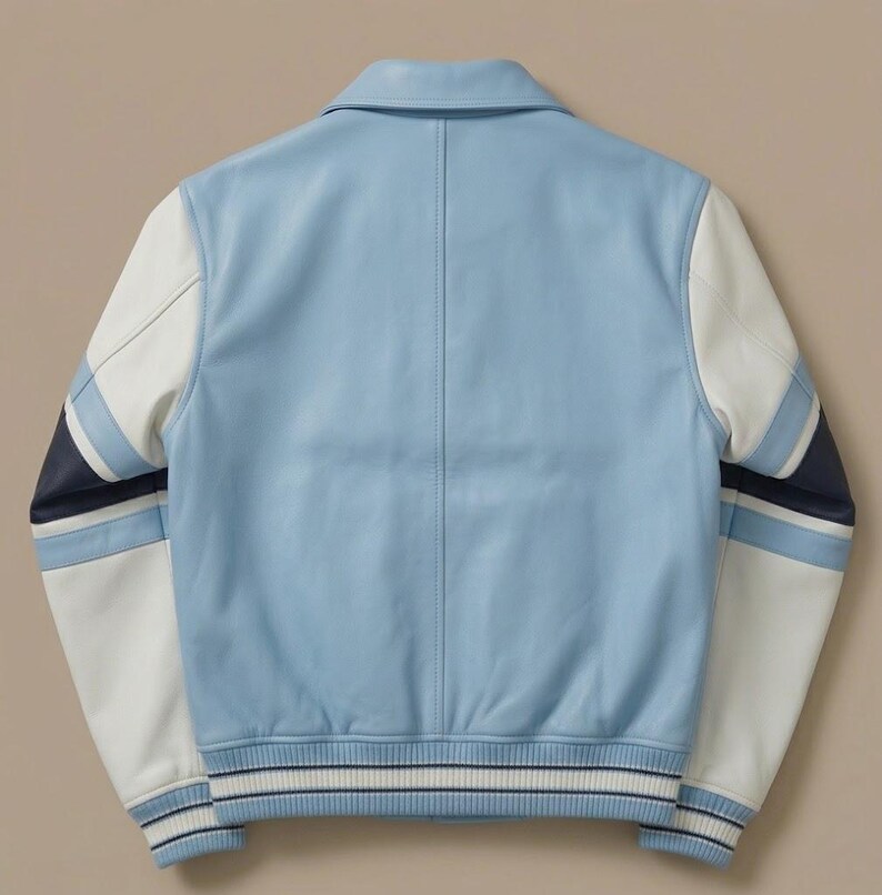 Puede incluir: Una chaqueta universitaria de color azul claro con mangas de cuero blanco y detalles de rayas en azul marino y azul claro. La chaqueta cuenta con un cuello cl&aacute;sico, dobladillo acanalado y pu&ntilde;os acanalados con rayas azul marino y blancas, vista trasera.