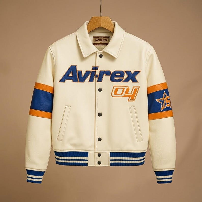 May include: An off-white varsity jacket featuring the text Avirex and 04 on the chest. The sleeves have blue and orange stripes with a star emblem on the left arm. It includes a pointed collar, snap button closure, and blue ribbed cuffs and hem.