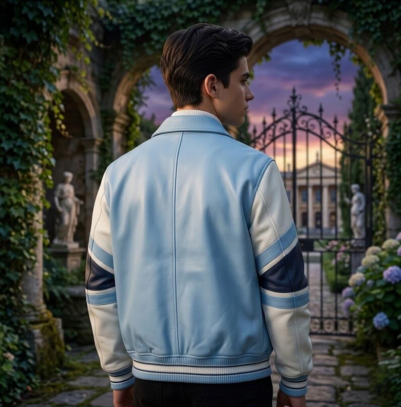Puede incluir: Una chaqueta universitaria de color azul claro con mangas blancas que presentan detalles de rayas en azul marino y azul claro. La chaqueta tiene cuello, pu&ntilde;os y dobladillo acanalados con rayas blancas y azul marino. Vista trasera de textura lisa.