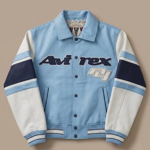 Puede incluir: Una chaqueta estilo varsity de color azul claro con mangas de bloques de color blanco y azul marino. El frente muestra el texto Avi-rex en azul oscuro y un parche blanco con el n&uacute;mero 41. Tiene cuello cl&aacute;sico, cierre de botones y pu&ntilde;os acanalados.