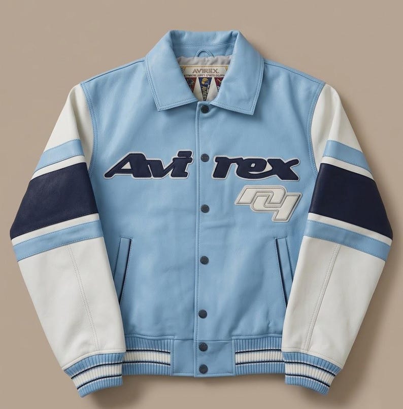 Puede incluir: Una chaqueta estilo varsity de color azul claro con mangas de bloques de color blanco y azul marino. El frente muestra el texto Avi-rex en azul oscuro y un parche blanco con el n&uacute;mero 41. Tiene cuello cl&aacute;sico, cierre de botones y pu&ntilde;os acanalados.