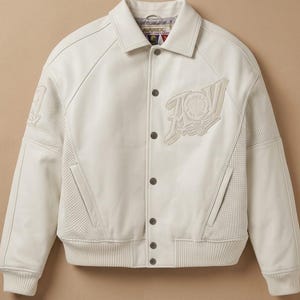 May include: Cream-colored leather jacket with a button-up front, collar, and ribbed cuffs. Features a large embroidered logo on the chest and perforated panels on the sleeves. A stylish outerwear piece.