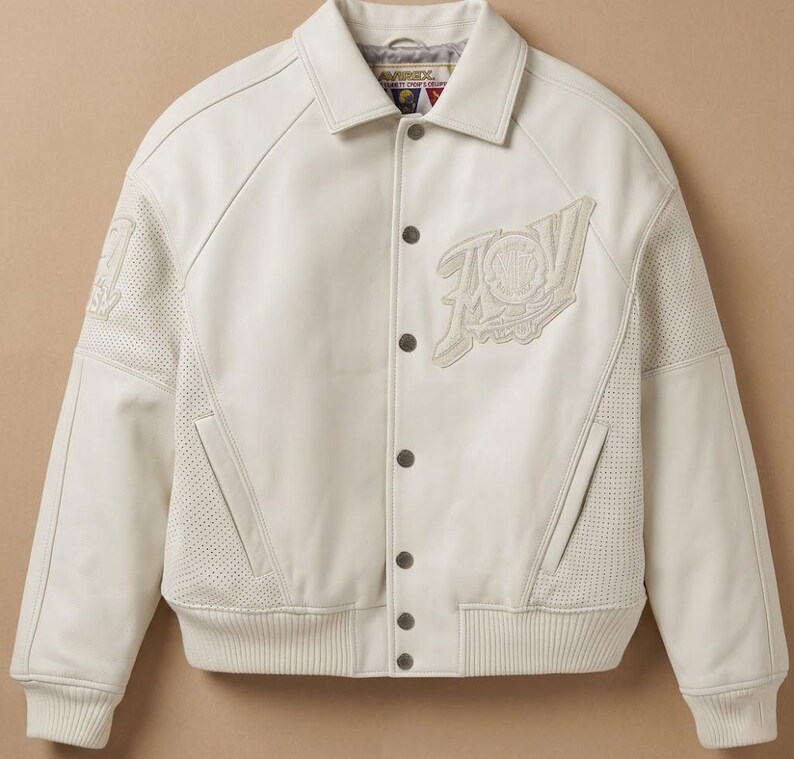 May include: Cream-colored leather jacket with a button-up front, collar, and ribbed cuffs. Features a large embroidered logo on the chest and perforated panels on the sleeves. A stylish outerwear piece.