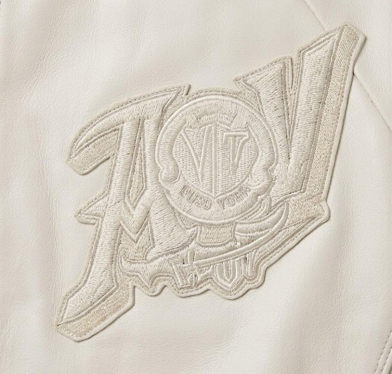 May include: Cream-colored embroidered patch with the letters "AV" and a circular emblem featuring "VT" and the words "PUSO YORK". The patch is sewn onto a cream-colored leather-like material.