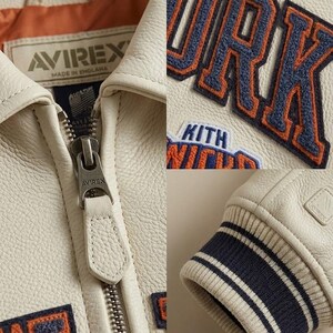 May include: Cream-colored leather jacket with the word "YORK" in navy and orange lettering. The jacket features a zipper closure, ribbed cuffs with navy and white stripes, and the brand "AVIREX" is visible.