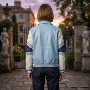 Puede incluir: Una chaqueta universitaria de cuero azul claro con mangas a rayas blancas y azul oscuro, cuello puntiagudo y dobladillo acanalado con rayas blancas y azul oscuro, usada con jeans azul oscuro, vista desde atr&aacute;s.