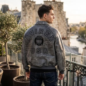 May include: A grey leather bomber jacket with a textured crocodile-skin pattern. The back features the black embroidered text AVIREX and USA, along with a circular patch displaying a flag graphic and the text ALL AMERICAN ESTABLISHED 1975.