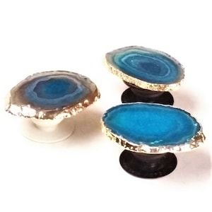May include: Three teal blue agate phone grips with gold trim. Each grip has a different pattern of blue and white agate.