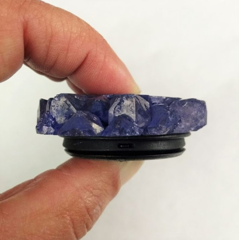 May include: A purple crystal phone grip with a black base. The crystal is shaped like a cluster of small crystals.