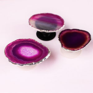 May include: Three purple agate phone grips with silver trim. The grips are round and have a raised center. They are on a white background.