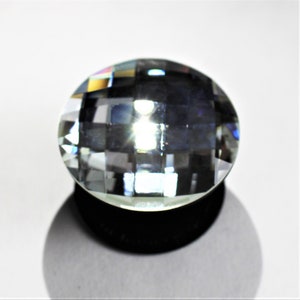 May include: A clear glass crystal with a faceted design, reflecting light in a rainbow of colors. The crystal is mounted on a black base.