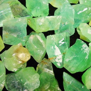 May include: A collection of green apatite crystal roughs. The crystals are translucent and have a variety of shapes and sizes.