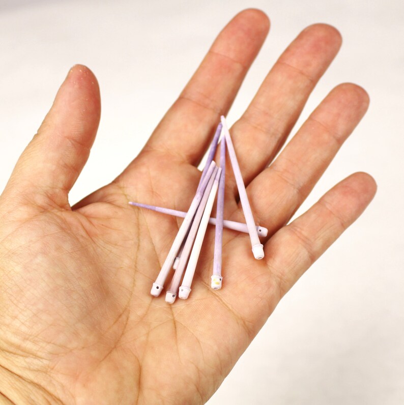 May include: A group of eight purple and white toothpicks are arranged in a fan shape in the palm of a hand.