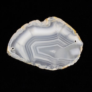 May include: A white agate slice with a natural, organic shape and intricate banding patterns. The slice has two drilled holes for hanging or stringing.