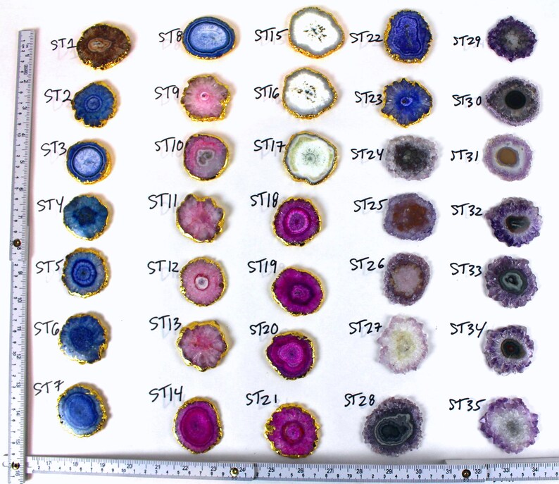 May include: Thirty-five agate slices with gold trim, arranged in rows on a white background. Each slice has a unique pattern of colors, including blue, purple, pink, and white.
