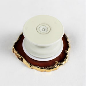 May include: A white phone grip with a gold-rimmed agate base. The grip has a round, white button in the center.