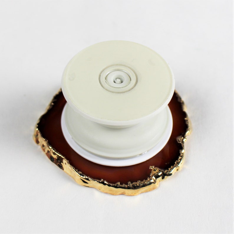 May include: A white phone grip with a gold-rimmed agate base. The grip has a round, white button in the center.